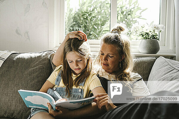 Daughter writing in book while sitting by mother on sofa at home
