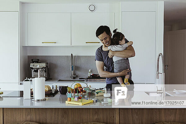 Smiling father carrying male toddler while standing by kitchen counter