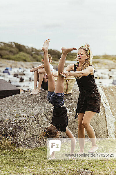 Mother helping daughter to do handstand on land at harbor
