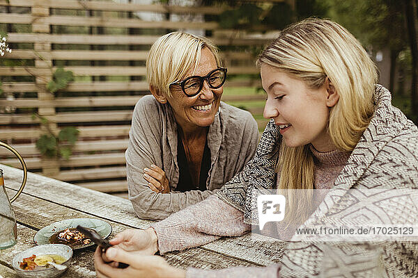 Glückliche Großmutter schaut auf Enkelin mit Handy im Hinterhof