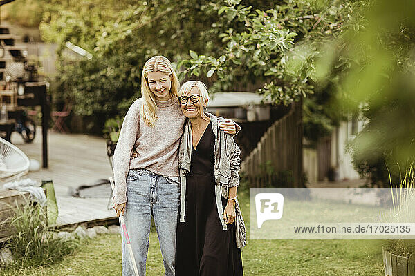 Lächelnde Enkelin mit Arm um Großmutter stehend im Hinterhof