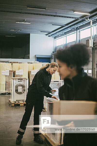 Businesswoman analyzing box containers with female manual worker at warehouse