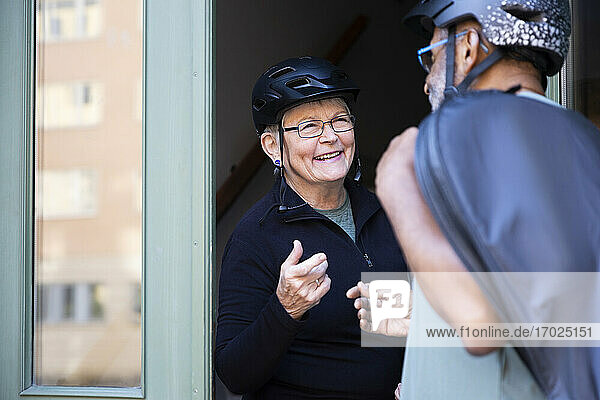 Lächelndes Seniorenpaar mit Fahrradhelm an der Eingangstür zu Hause