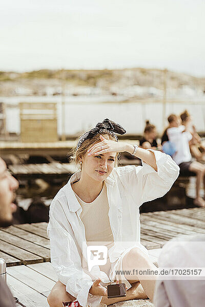 Junge Frau Abschirmung Augen beim Sitzen mit Freunden während Picknick am sonnigen Tag