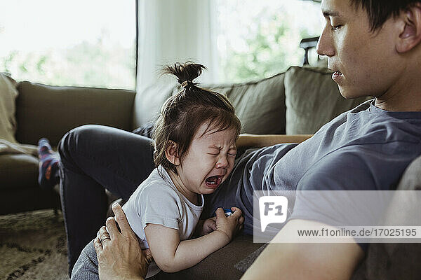 Vater im Vaterschaftsurlaub schaut auf weinendes Kleinkind im Wohnzimmer