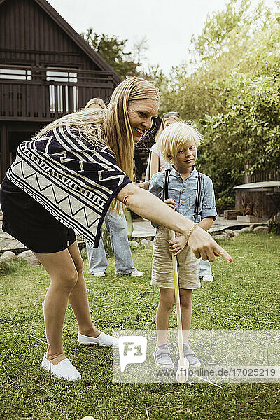 Mutter zeigt  während sie bei ihrem Sohn steht  der im Vorgarten Polo spielt