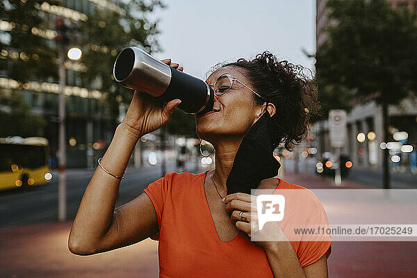 Smiling businesswoman drinking coffee in city during COVID-19
