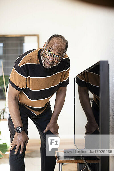 Älterer Mann schaut weg  während er zu Hause vor dem Fernseher steht