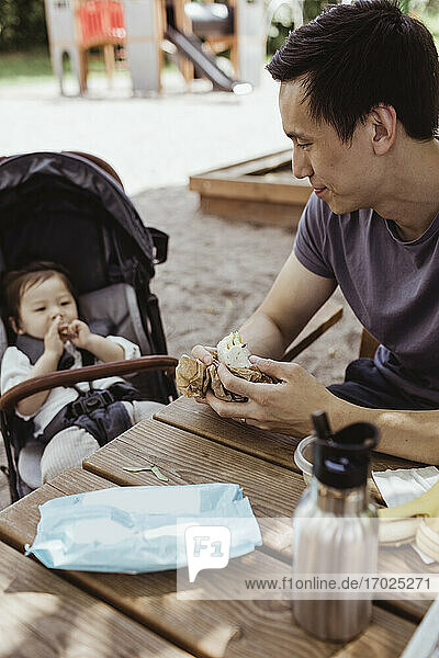 Vater füttert männliches Kleinkind beim Sitzen auf dem Spielplatz