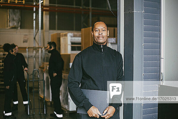 Confident male entrepreneur standing with clipboard at logistics warehouse
