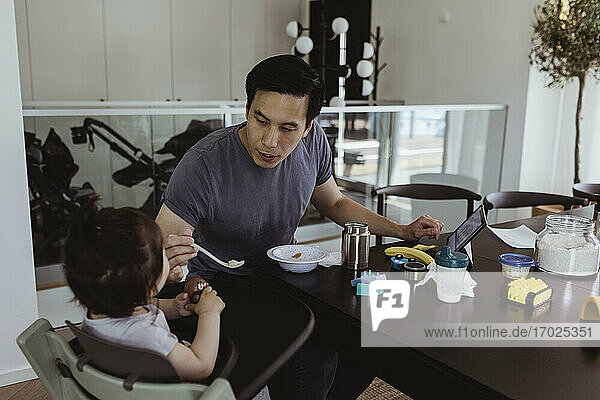 Vater füttert männliches Kleinkind über Tisch zu Hause