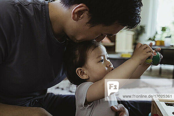 Männliches Kleinkind spielt  während der Vater den Kopf im Wohnzimmer küsst