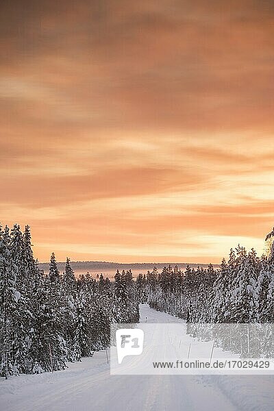 Eisige  schneebedeckte Winterstraße am Polarkreis bei Sonnenuntergang in Lappland  Finnland