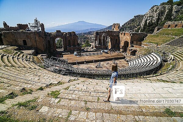 Taormina Greek Theatre aka Teatro Greco  tourist at the amphitheatre with Mount Etna Volcano behind  Sicily  Italy  Europe. This is a photo of a tourist at Teatro Greco aka Taormina Greek Theatre or Amphitheatre  with Mount Etna Volcano in the background  Sicily  Italy  Europe.