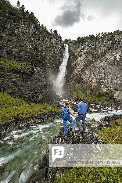 Two hikers  couple  standing on rocks by river Driva  Svøufallet waterfall  Åmotan gorge  Gjøra  Norway  Europe