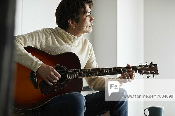Japanese man playing guitar at home