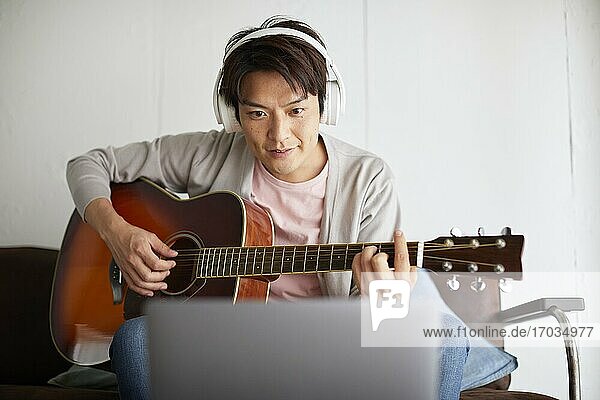 Japanese man playing guitar at home