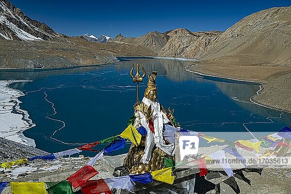 Tilicho Lake covered with ice in front of mountain scenery with Buddhist prayer flags and Hindu Shiva statue  often called the highest lake in the world  Annapurna region  4919 m altitude  Himalaya  Nepal  Asia