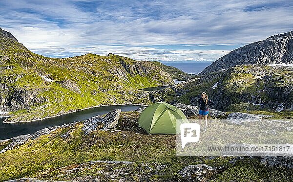 Wanderin steht neben Zelt in den Bergen  bei Sørvågen  Moskenesøya  Lofoten  Nordland  Norwegen  Europa
