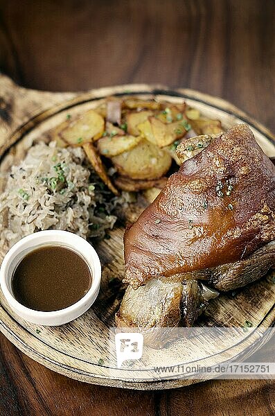 SCHWEINSHAXE traditionelle deutsche Schweinshaxe mit Sauerkraut und Kartoffeln bayerische Mahlzeit auf rustikalem Holz Hintergrund., SCHWEINSHAXE traditionelle deutsche Schweinshaxe mit Sauerkraut und Kartoffeln bayerische Mahlzeit auf rustikalem Holz Hintergrund.