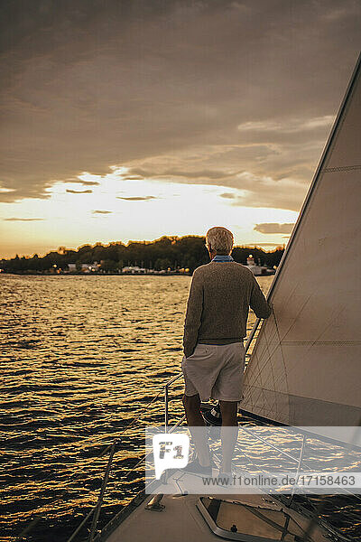 Rückansicht eines älteren Mannes  der das Meer bei Sonnenuntergang bewundert