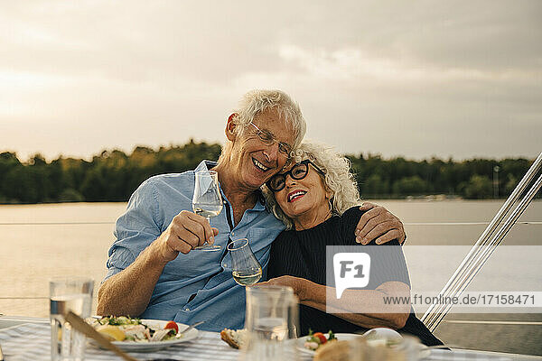 Glücklicher älterer Mann mit Arm um Frau mit Wein gegen Meer in Boot