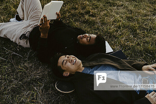 Junger Mann liest Tagebuch liegend bei männlichem Freund auf Gras im Park