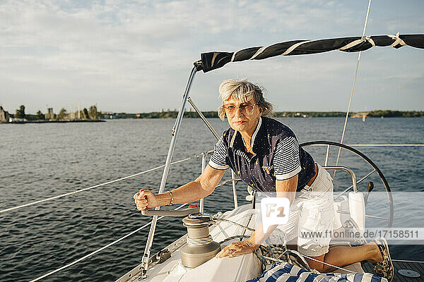Ältere Frau dreht Griff beim Segeln Boot im Meer am sonnigen Tag