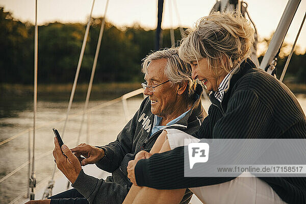 Lächelndes heterosexuelles Paar mit Smartphone bei Sonnenuntergang