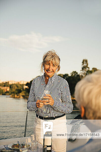 Lächelnde ältere Frau mit Weinglas schaut auf Mann in Boot gegen Himmel