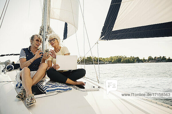 Senior weibliche Freunde mit Smartphone beim Sitzen auf Boot während sonnigen Tag