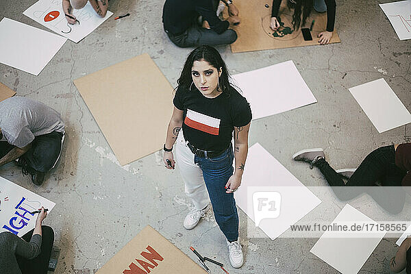 Porträt einer stehenden Frau  während ein männlicher und ein weiblicher Aktivist Schilder in einem Gebäude vorbereiten
