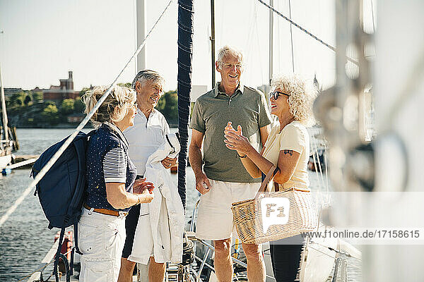Männliche und weibliche ältere Freunde im Gespräch miteinander  während in Boot auf sonnigen Tag stehen
