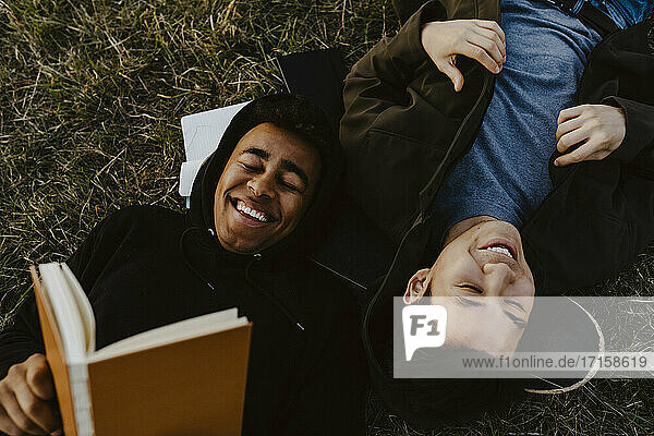 Glücklicher Mann mit Tagebuch liegend von männlichen Freund auf Gras im Park