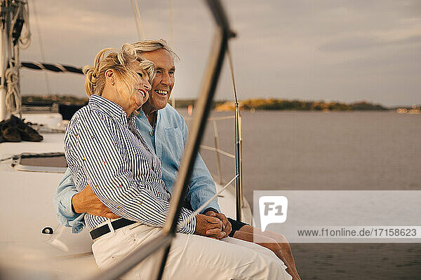 Glückliche Senior Paar sitzt auf dem Rand des Segelbootes während des Sonnenuntergangs