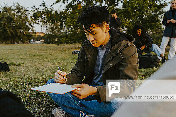 Junger Mann schreibt in Buch im Park