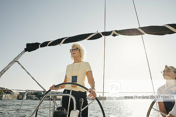 Senior woman sailing boat with female friend against clear sky on sunny day