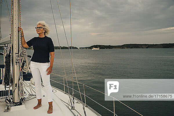Ältere Frau schaut weg  während sie in einem Boot gegen den Himmel und das Meer bei Sonnenuntergang steht