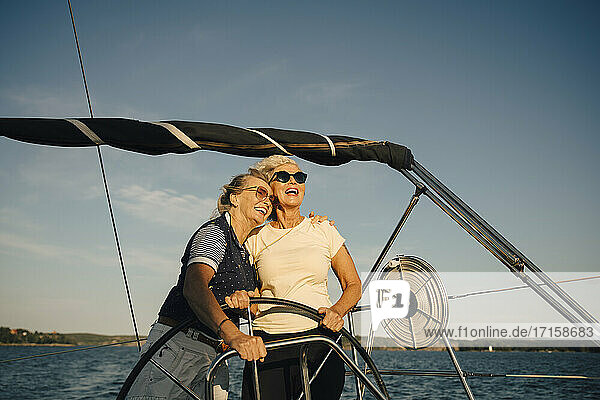 Fröhliche Freundinnen schauen weg  während sie in einem Boot gegen den Himmel stehen