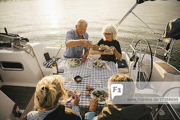 Glückliche ältere Mann mit geschnittenem Brot mit Freunden in Boot auf sonnigen Tag