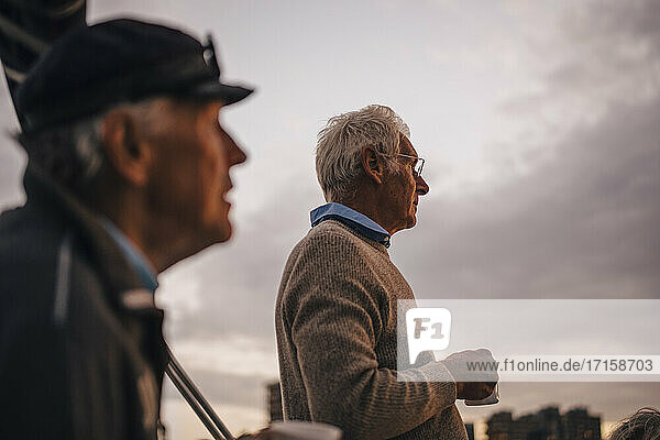 Männliche Freunde mit Kaffeetasse Blick weg gegen Himmel während Sonnenuntergang
