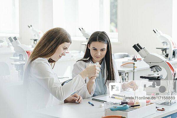 Young female researchers in white coats examining laboratory sample in science class