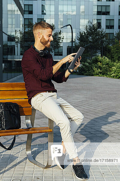 Unternehmer  der ein digitales Tablet benutzt  während er auf einer Bank sitzt