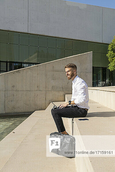 Businessman using digital tablet while sitting on steps during sunny day