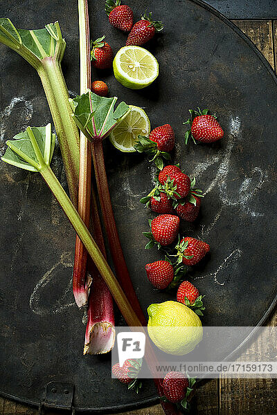 Frischer Rhabarber  Erdbeeren  Zitrone und Limette auf rustikalem Backblech