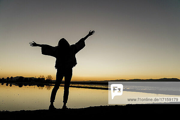 Young woman with arms outstretched standing by river during dusk at Ebro delta  Spain