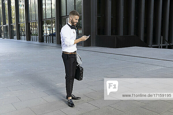 Businessman with briefcase using mobile phone while standing on footpath