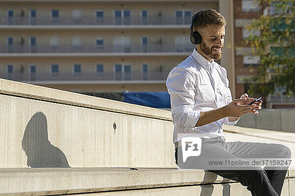 Mid adult businessman smiling while using smart phone sitting on steps