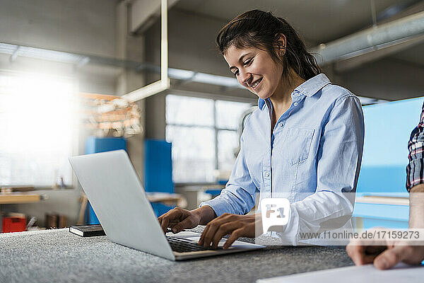 Smiling businesswoman working on laptop while standing by colleague at industry