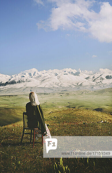 Woman sitting on chair while looking at view against cloudy sky